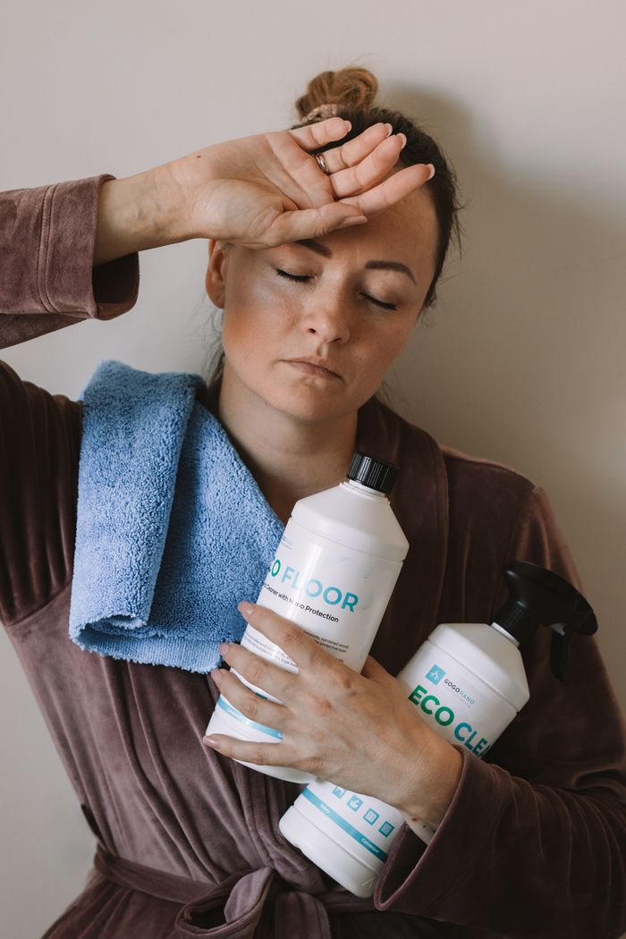 hero-01 Woman holding eco-friendly cleaning products with blue microfiber cloth indoors.